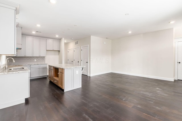 kitchen with decorative backsplash, light stone counters, a center island, and sink