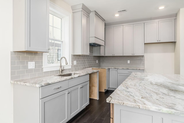 kitchen with light stone countertops, tasteful backsplash, gray cabinetry, dark wood-type flooring, and sink