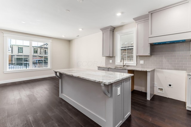 kitchen with a center island, sink, gray cabinets, tasteful backsplash, and light stone counters