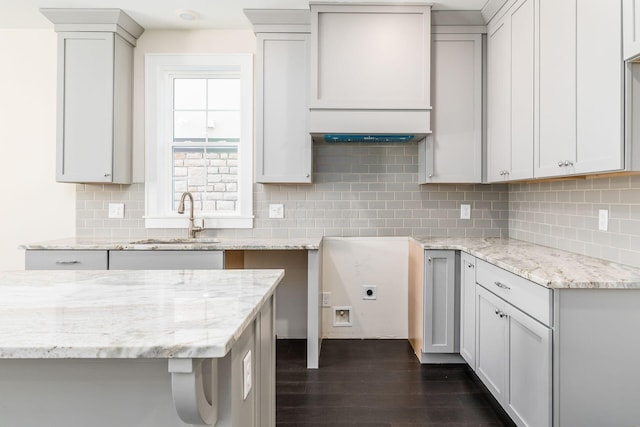 kitchen featuring decorative backsplash, dark hardwood / wood-style floors, light stone counters, and sink