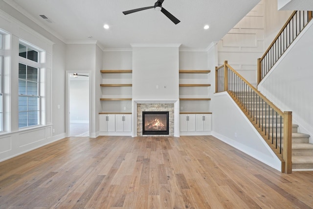 unfurnished living room featuring a fireplace, ceiling fan, crown molding, built in shelves, and light hardwood / wood-style flooring