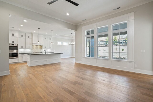 unfurnished living room with ornamental molding, sink, ceiling fan with notable chandelier, and light wood-type flooring