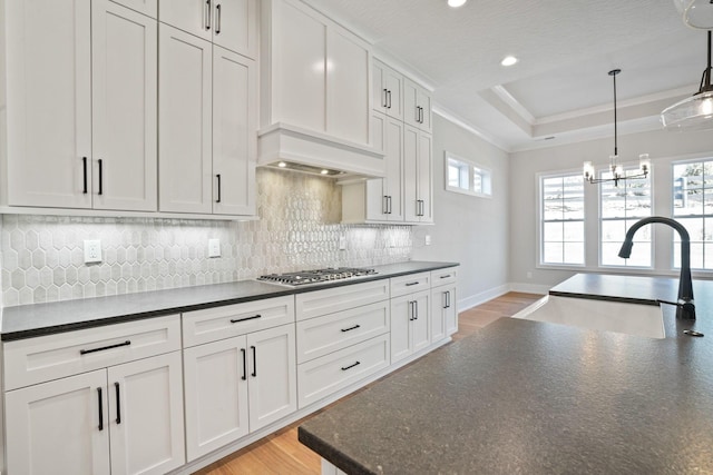 kitchen with sink, light hardwood / wood-style floors, white cabinets, decorative light fixtures, and a raised ceiling