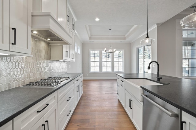 kitchen with premium range hood, appliances with stainless steel finishes, decorative light fixtures, sink, and a tray ceiling