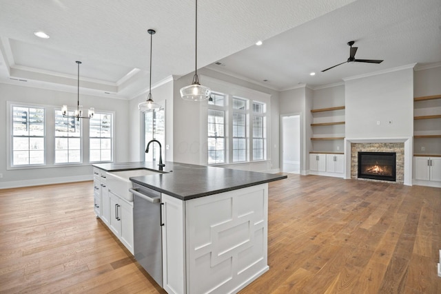 kitchen with hanging light fixtures, light wood-type flooring, a center island with sink, stainless steel dishwasher, and white cabinets