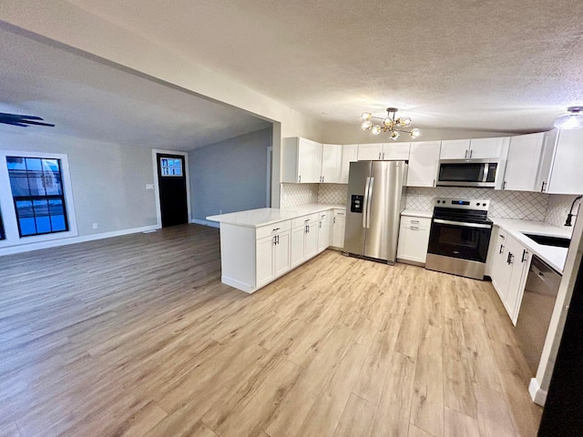 kitchen with tasteful backsplash, kitchen peninsula, appliances with stainless steel finishes, white cabinets, and a chandelier