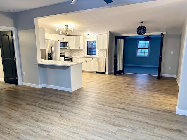 kitchen featuring kitchen peninsula, appliances with stainless steel finishes, backsplash, white cabinets, and light hardwood / wood-style flooring