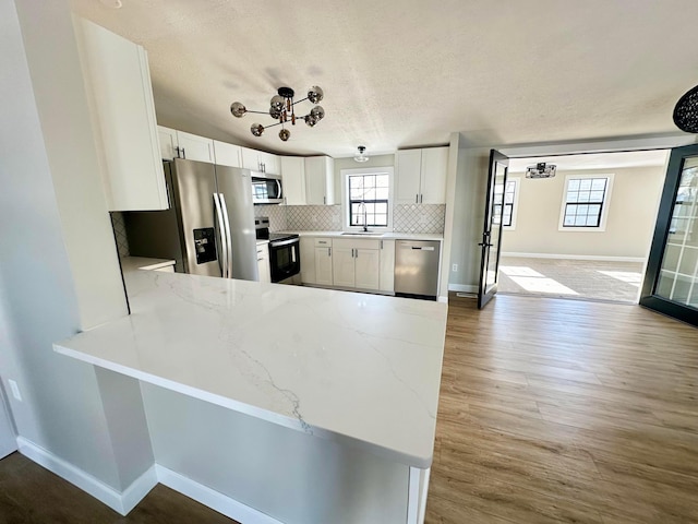 kitchen featuring tasteful backsplash, kitchen peninsula, stainless steel appliances, white cabinets, and light stone counters