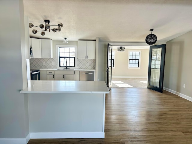 kitchen with tasteful backsplash, decorative light fixtures, kitchen peninsula, appliances with stainless steel finishes, and white cabinets