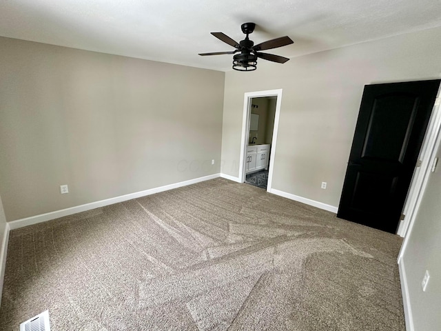 unfurnished bedroom with ceiling fan, ensuite bath, and dark colored carpet