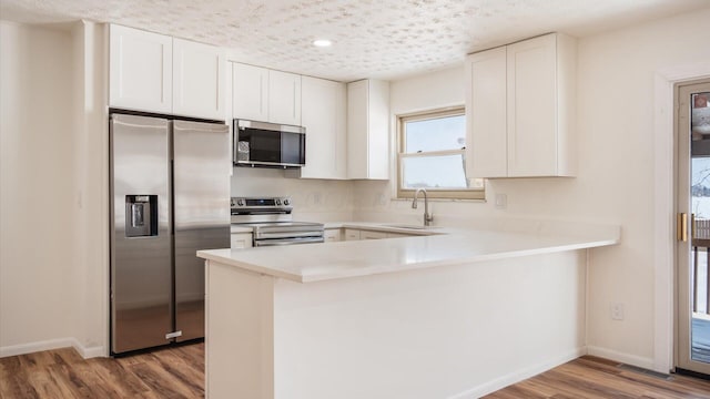 kitchen with kitchen peninsula, stainless steel appliances, sink, white cabinets, and light hardwood / wood-style floors