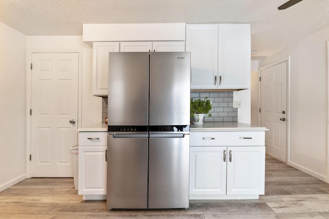 kitchen with white cabinets, backsplash, stainless steel fridge, and light wood-type flooring