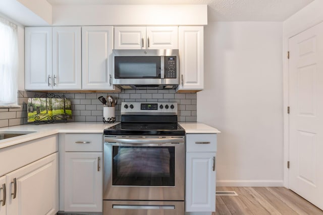 kitchen with light hardwood / wood-style floors, white cabinetry, decorative backsplash, and stainless steel appliances