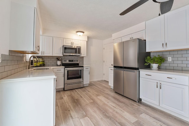 kitchen featuring ceiling fan, sink, light wood-type flooring, stainless steel appliances, and white cabinets