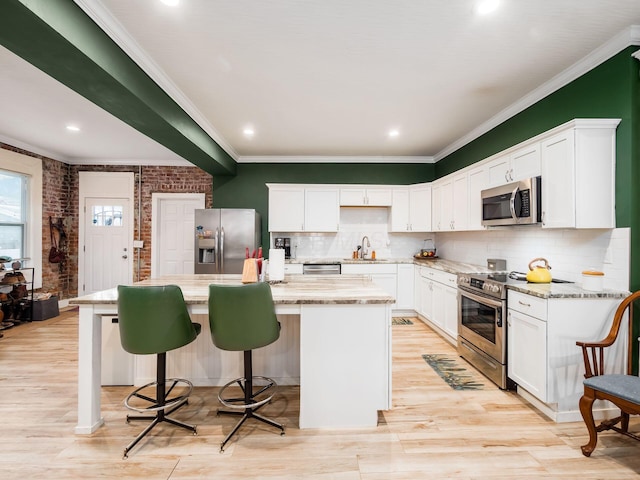 kitchen with white cabinetry, brick wall, a center island with sink, and appliances with stainless steel finishes