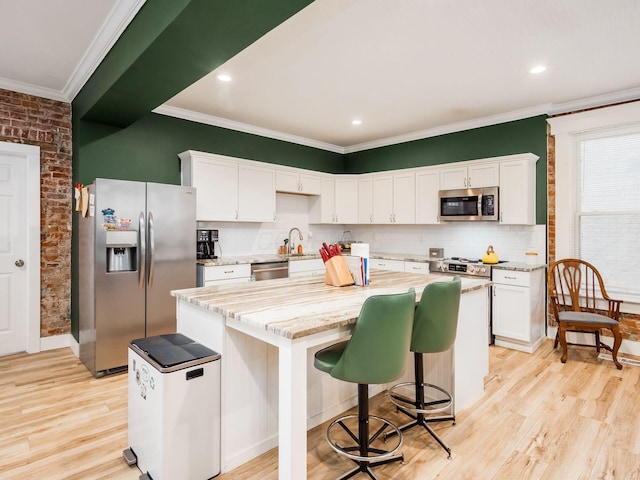 kitchen featuring white cabinets, a kitchen island, brick wall, and appliances with stainless steel finishes