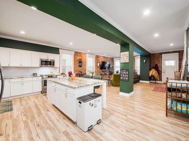 kitchen featuring a kitchen island, white cabinetry, brick wall, and appliances with stainless steel finishes