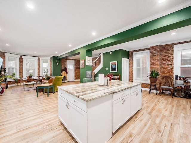 kitchen with crown molding, light stone countertops, white cabinets, light wood-type flooring, and a kitchen island