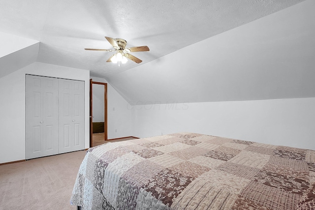 bedroom with lofted ceiling, light carpet, ceiling fan, a textured ceiling, and a closet