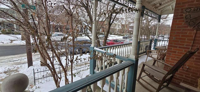 snow covered back of property featuring covered porch