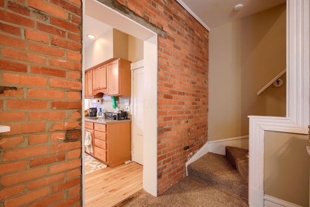 kitchen with light brown cabinetry, light carpet, and brick wall