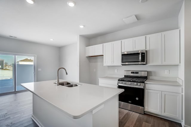 kitchen featuring wood finished floors, a center island with sink, a sink, stainless steel appliances, and white cabinetry