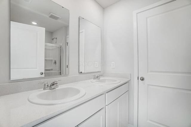 bathroom with double vanity, visible vents, a shower with shower door, and a sink