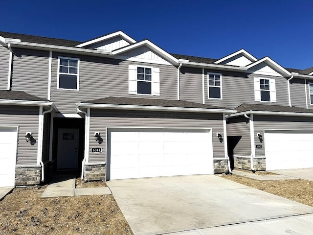 townhome / multi-family property with a garage, stone siding, and driveway