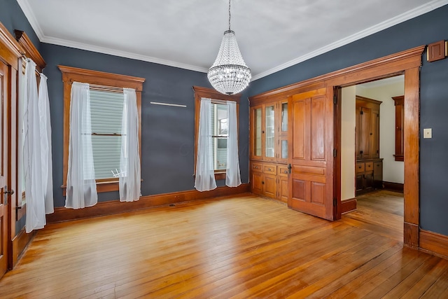 unfurnished dining area featuring ornamental molding, light wood-type flooring, and a notable chandelier