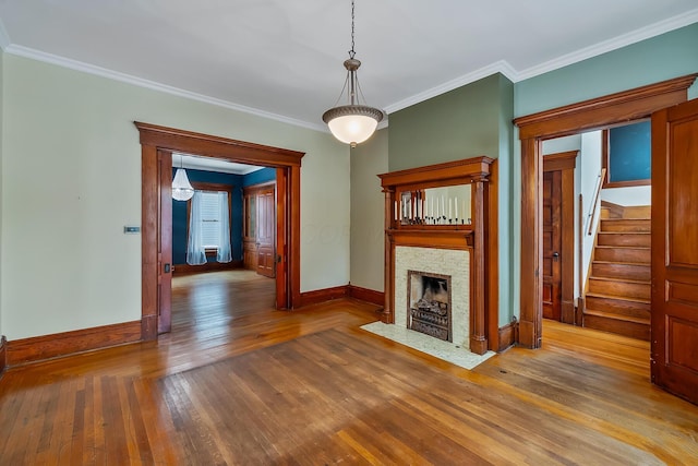 unfurnished living room featuring a stone fireplace, crown molding, and wood-type flooring