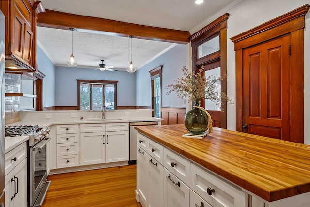 kitchen with wood counters, white cabinets, sink, hanging light fixtures, and stainless steel appliances