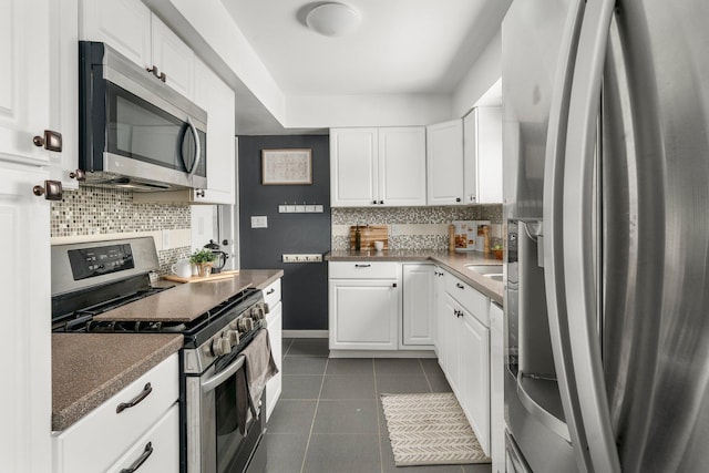 kitchen with stainless steel appliances, dark tile patterned floors, white cabinets, and decorative backsplash