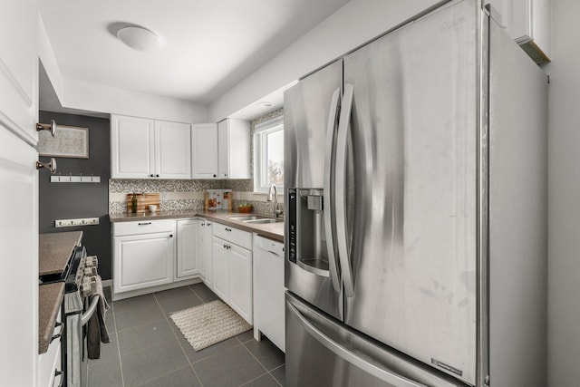 kitchen with stainless steel appliances, dark tile patterned flooring, backsplash, white cabinetry, and sink