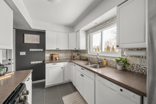 kitchen with white dishwasher, dark tile patterned flooring, decorative backsplash, sink, and white cabinetry