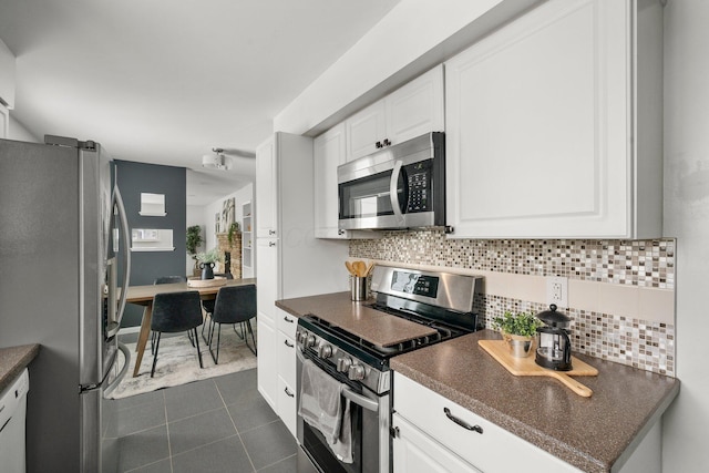 kitchen with stainless steel appliances, dark tile patterned floors, white cabinets, and tasteful backsplash