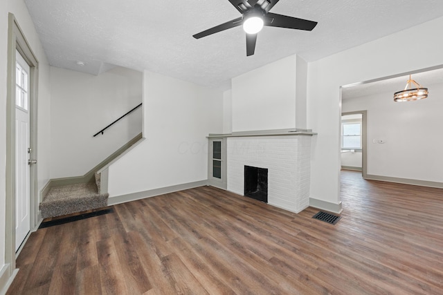 unfurnished living room featuring a textured ceiling, ceiling fan with notable chandelier, dark wood-type flooring, and a brick fireplace