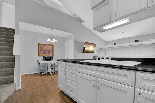 kitchen featuring sink, wood-type flooring, decorative light fixtures, a notable chandelier, and white cabinets