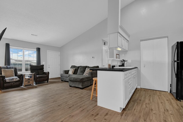 kitchen with kitchen peninsula, a kitchen breakfast bar, black fridge, and white cabinetry