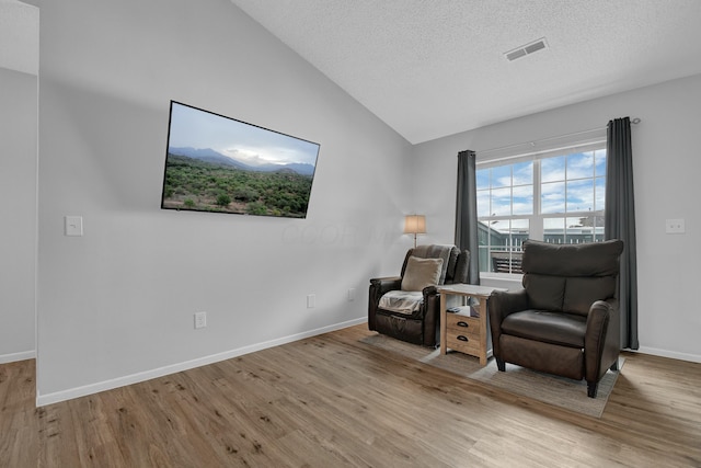 living area with lofted ceiling, light wood-type flooring, and a textured ceiling