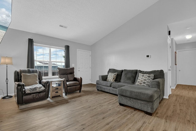 living room with a textured ceiling, light hardwood / wood-style floors, and vaulted ceiling