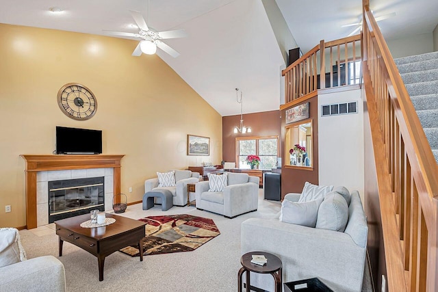 carpeted living room featuring ceiling fan with notable chandelier, a tile fireplace, and high vaulted ceiling