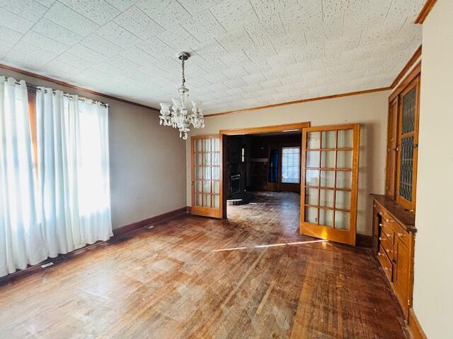 unfurnished dining area with french doors, ornamental molding, dark hardwood / wood-style floors, and a chandelier