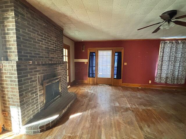 unfurnished living room with wood-type flooring, a brick fireplace, and ceiling fan