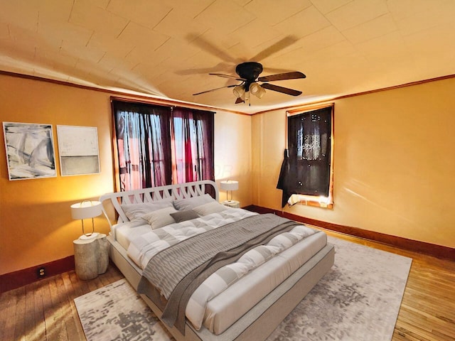 bedroom with ceiling fan, crown molding, baseboards, and wood-type flooring