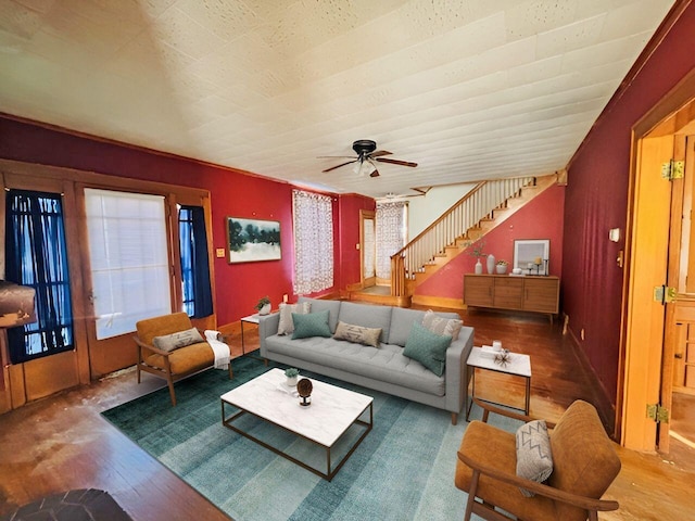 living area with a wealth of natural light, a ceiling fan, wood finished floors, and stairs