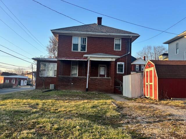 back of property featuring brick siding, a shed, covered porch, and central AC unit