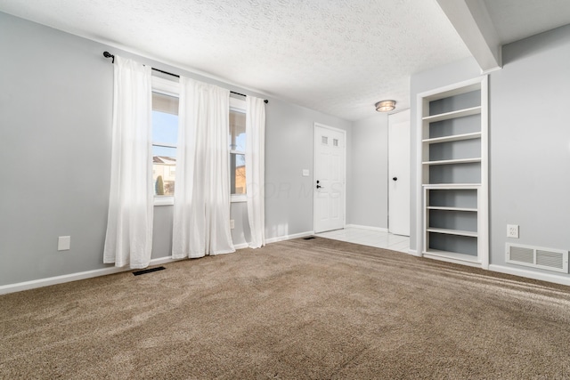 empty room featuring beam ceiling, built in shelves, carpet, and a textured ceiling