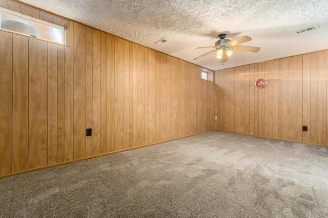 carpeted spare room with ceiling fan, a textured ceiling, and wooden walls