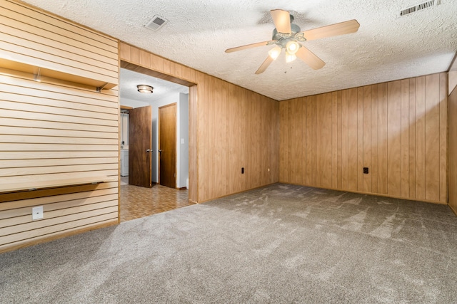 carpeted empty room featuring wooden walls, ceiling fan, and a textured ceiling