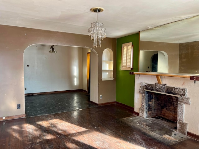 unfurnished living room with a chandelier, a fireplace, and dark wood-type flooring